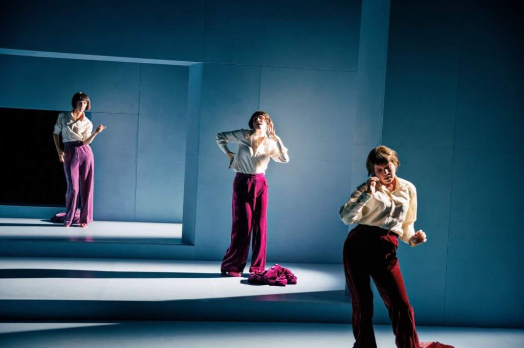 Drei Frauen in magenta-farbenen Hosen und weißen Blusen stehen wie gestaffelt auf Stufen.