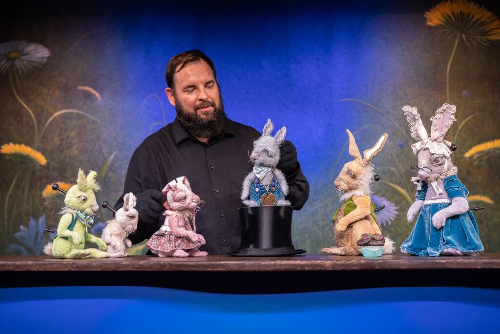 Ein Mann in Schwarz bewegt mehrere Hasen-Plüsch-Figuren.