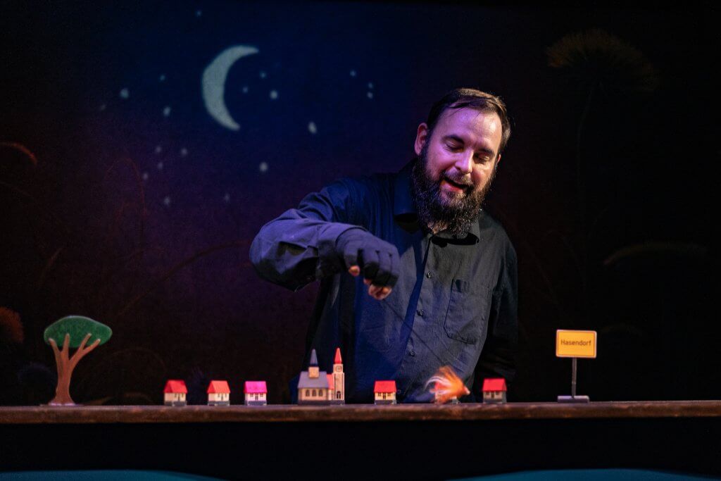 Ein Mann in Schwarz steht an einem Tisch mit kleinen Häuschen.