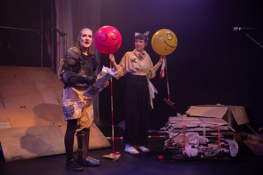 Zwei Personen stehen nebeneinander auf einer Bühne und halten jeweils einen Ballon in Pink und Gelb.