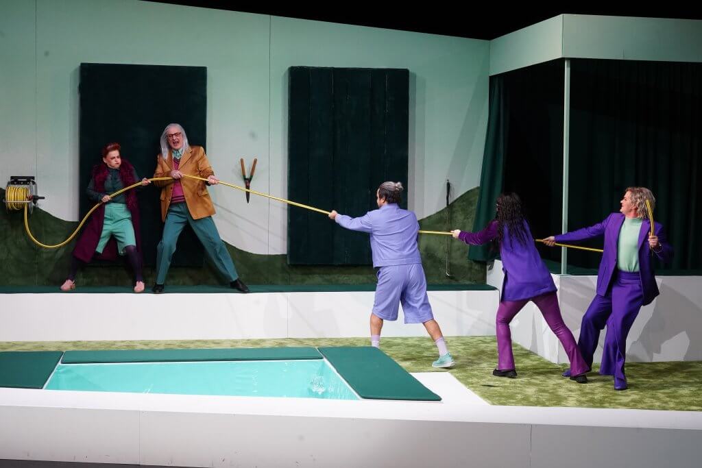 Eine Gruppe zieht an einem Seil über einem Pool - zwei auf der linken, drei auf der rechten Seite.