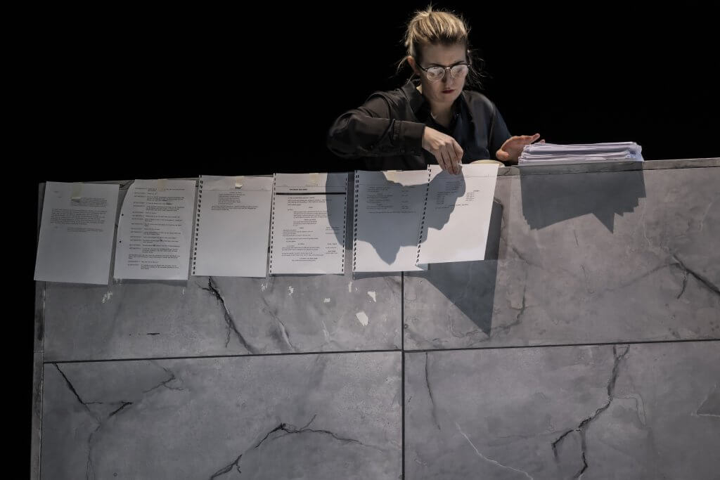 Eine Person schaut über eine Mauer auf einer Bühne und befestigt mehrere Zettel daran.