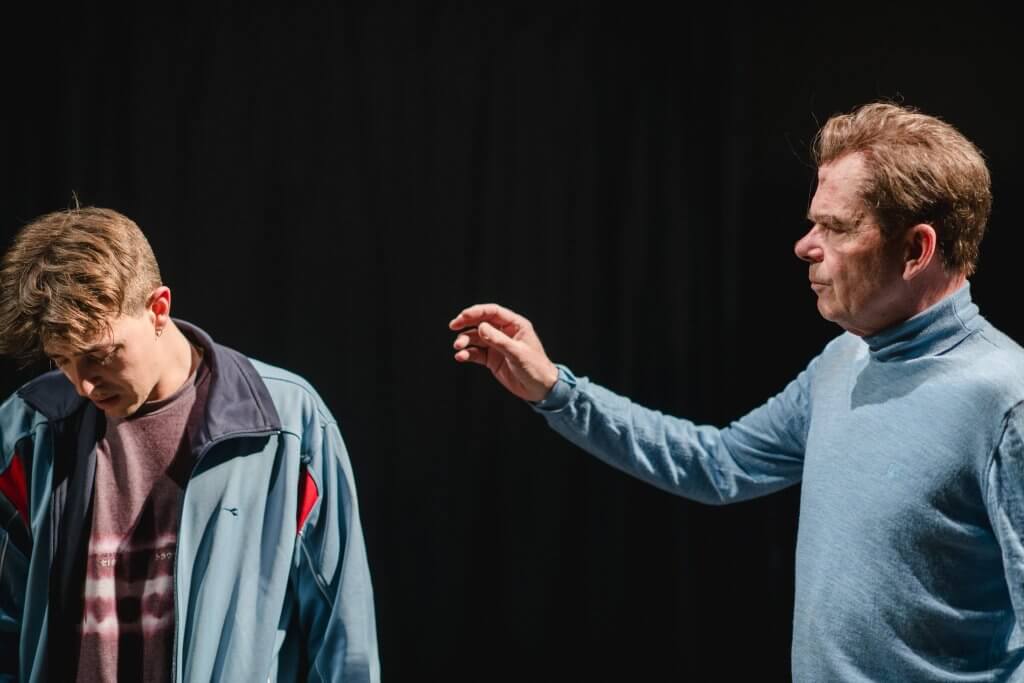 Ein Mann versucht vorsichtig einen Jungen mit weggedrehten Gesicht an der Schulter zu berühren.