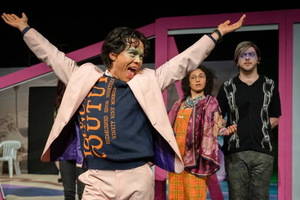 Eine Person in altrosa Anzug post dynamisch vor einer Gruppe Menschen.