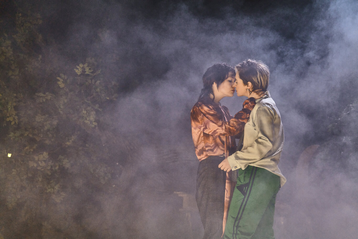 ein sich küssendes Paar vorne rechts, umgeben von Nebel