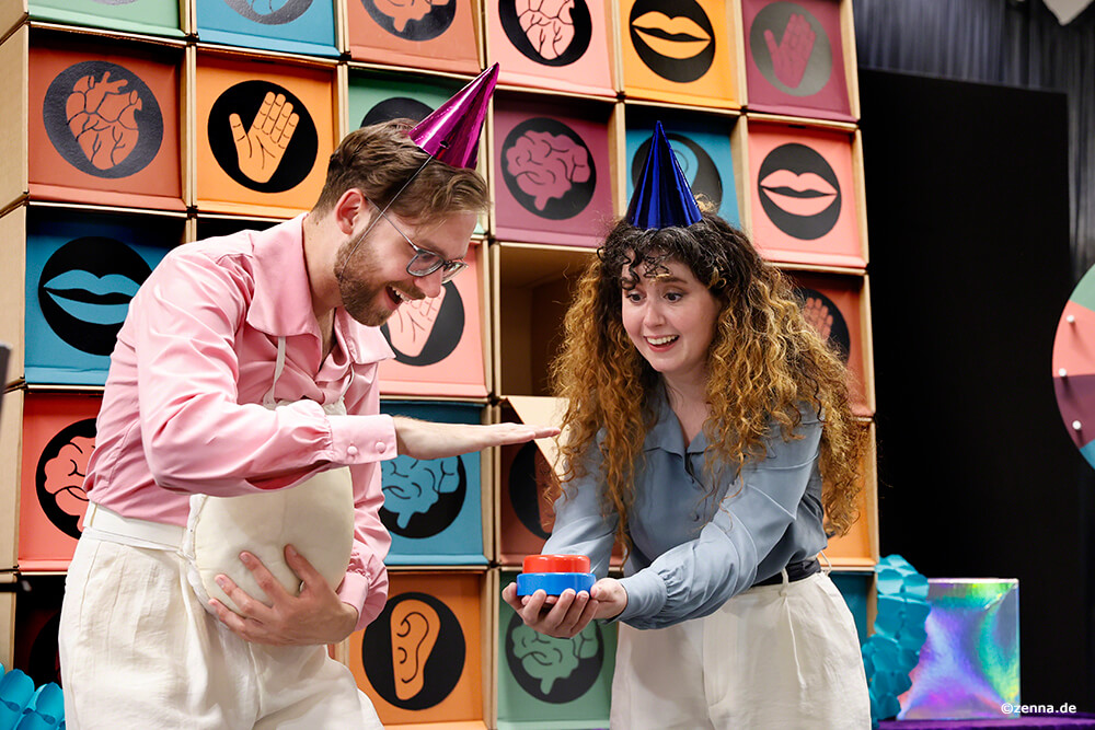 zwei Darsteller:innen mit Partyhütchen