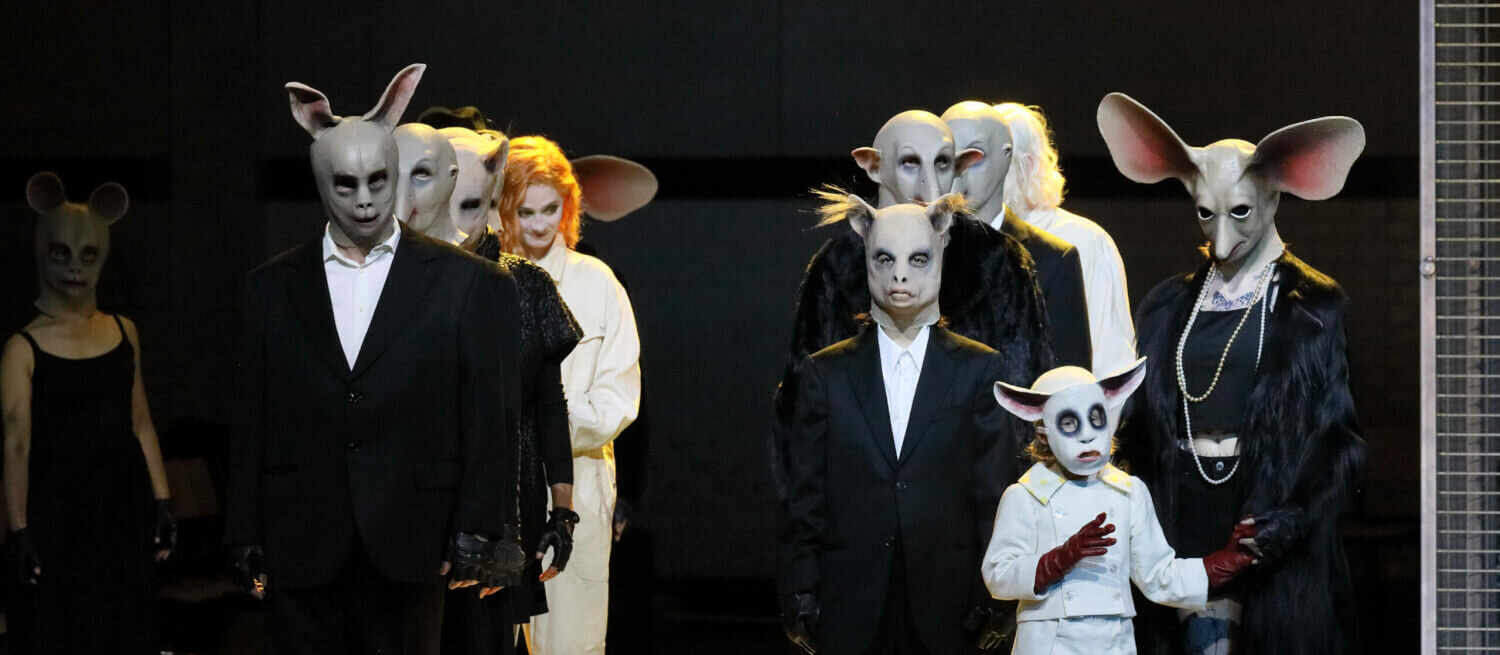 Das Ensemble steht in zwei Reihen auf der Bühne. Alle tragen unterschiedliche skurrile Tiermasken.