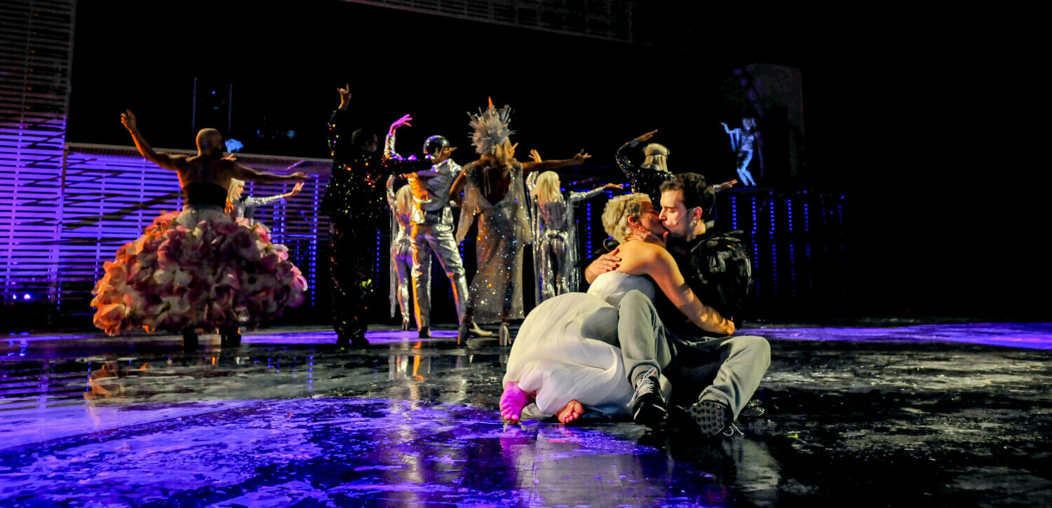 vorne ein küssendes Paar, im Hintergrund wuseliges Bühnengeschehen
