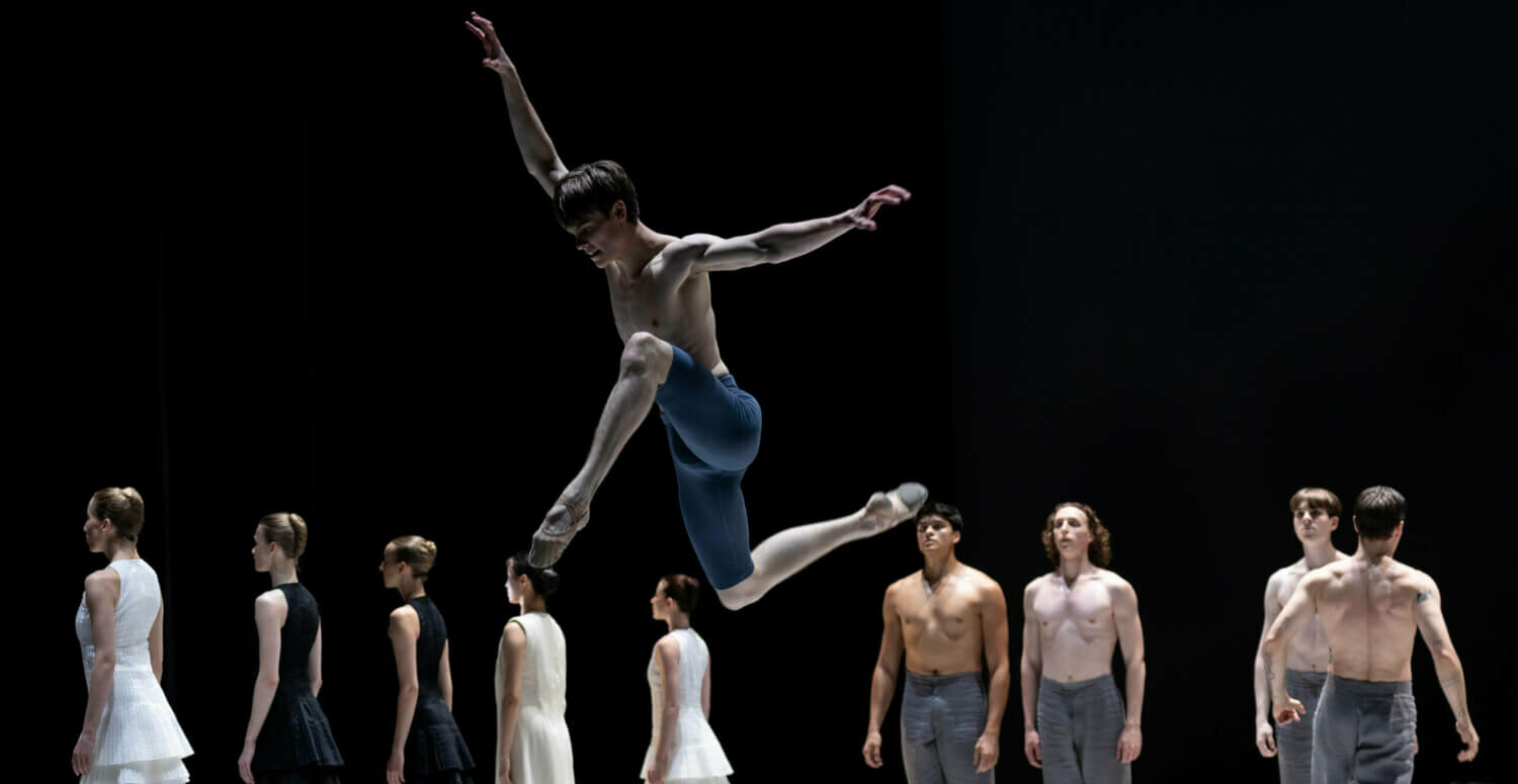 springender männlich gelesener Tänzer vor weiteren Tänzer:innen im Hintergrund