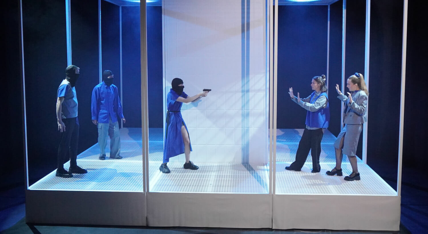 Drei Personen mit Strumpfmaske, eine davon bedroht mit Waffe zwei weitere Personen