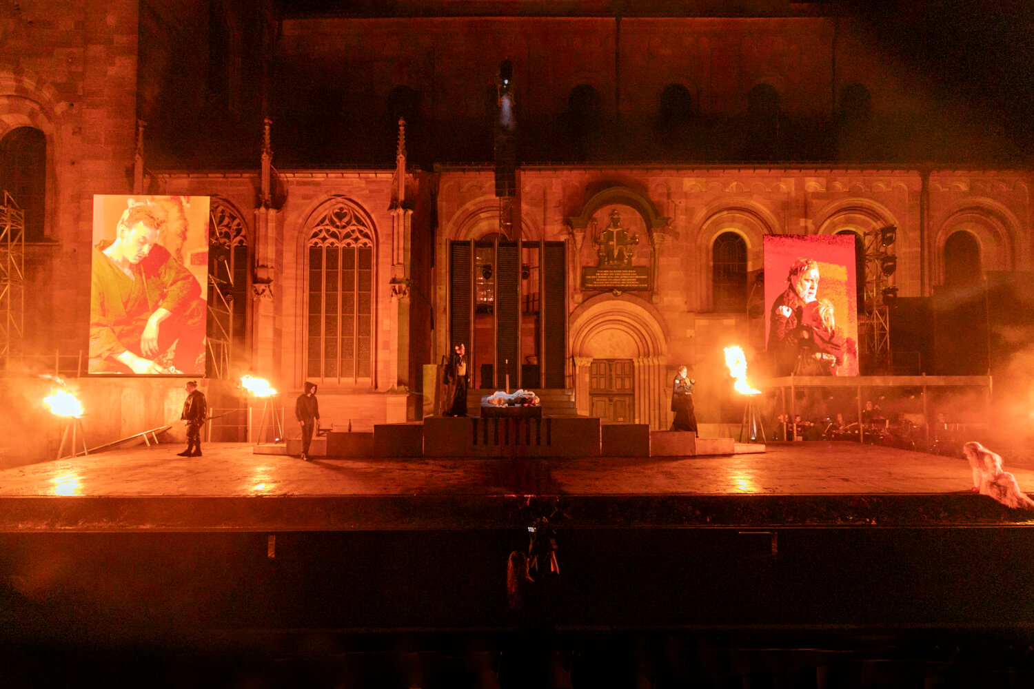 Das Ensemble steht vor einer bedrohlich in rot aufleuchtenden Kulisse.