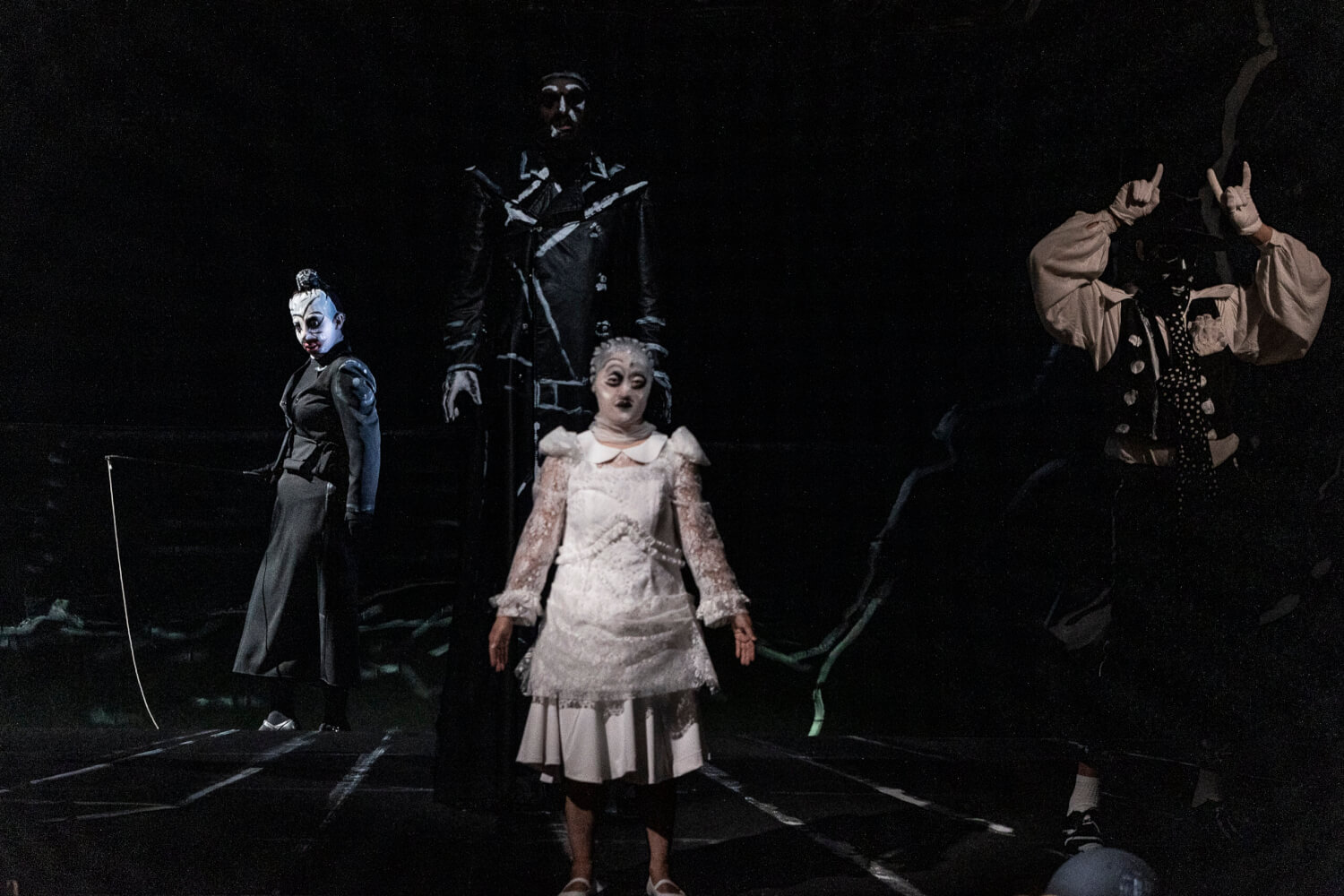 Drei Darsteller:innen stehen auf der Bühne, alle in leicht schaurig anmutende Kostüme gekleidet. Alles wirkt sehr düster und gruselig.