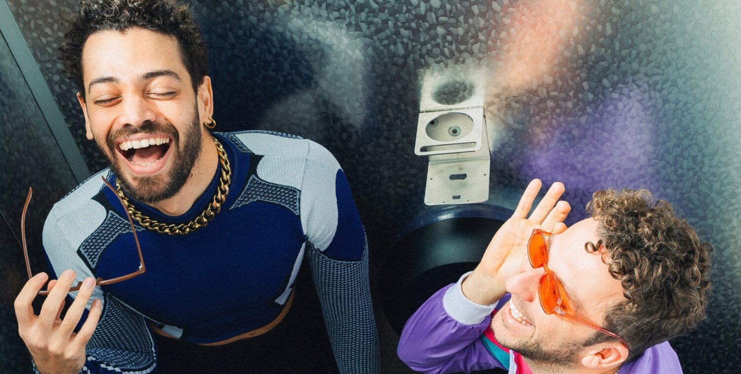 Zwei Personen in einer Klokabine, eine lacht, die andere fasst sich an die Sonnenbrille