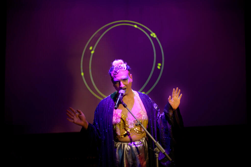 eine Person vor lila-blau beleuchtetem Hintergrund und vor einem Mikrofon