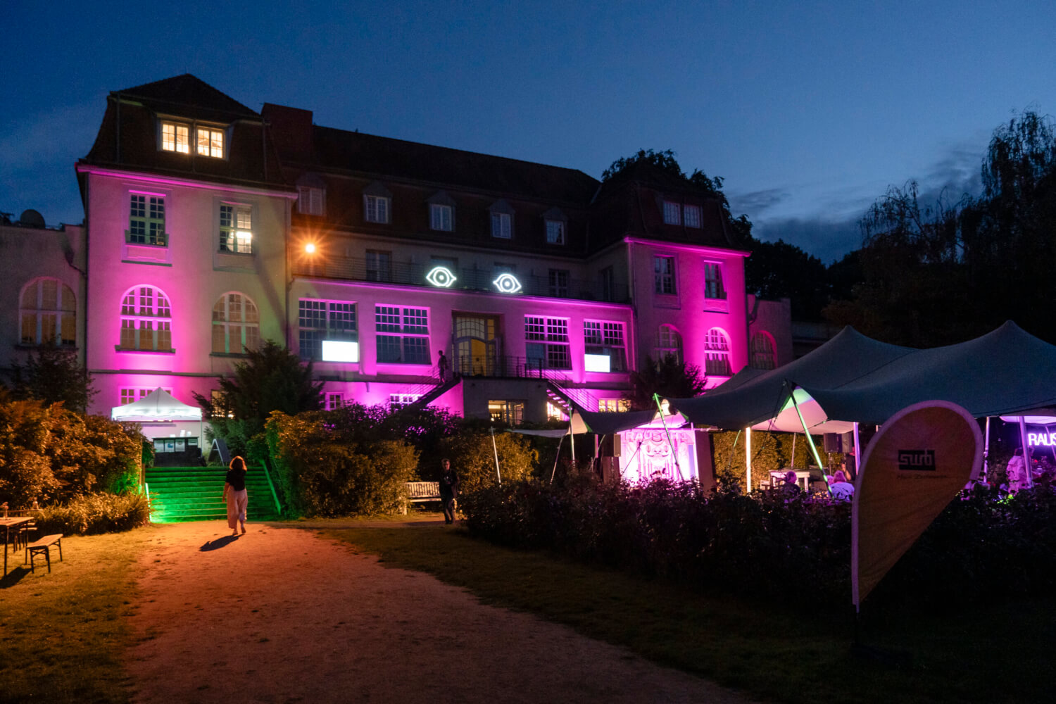 Zu sehen ist das Theater an der Ruhr in Mülheim, atmosphärisch in lila angestrahlt bei Nacht.