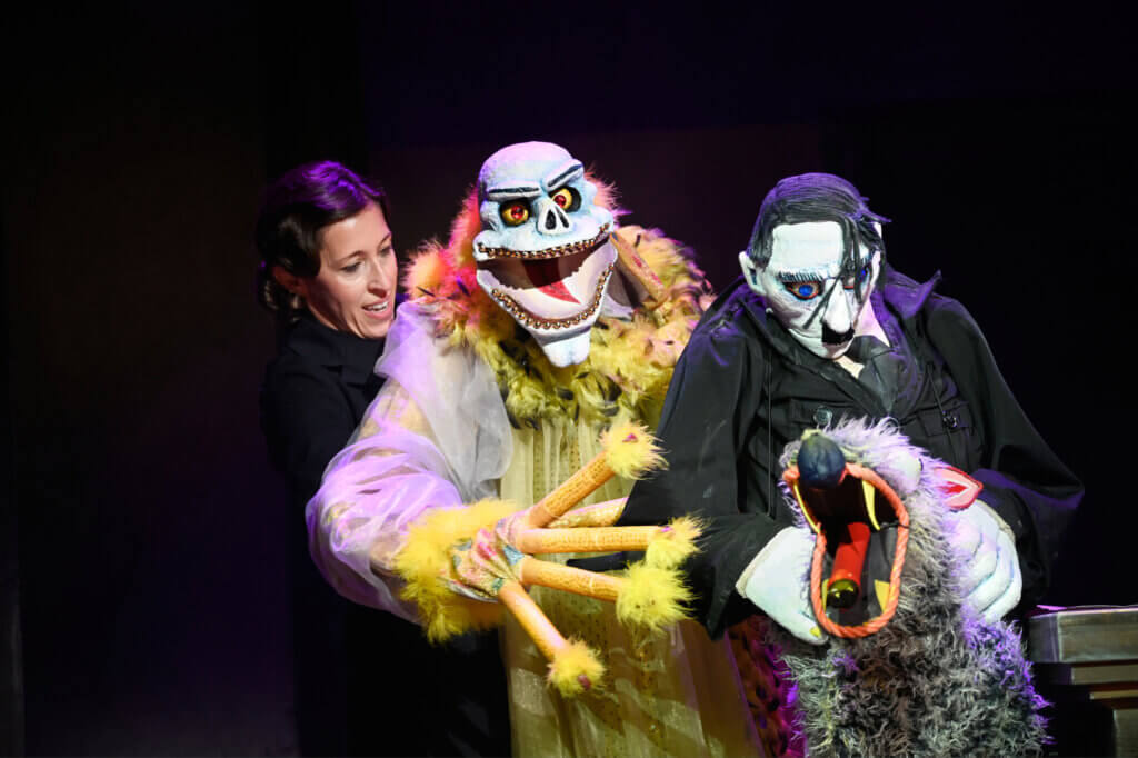 Eine Puppenspielerin mit einer lebensgroßen Puppe, die den Tod darstellt, daneben eine Adolf Hitler-Puppe und sein Schäferhund „Blondie“, ebenfalls als Puppe