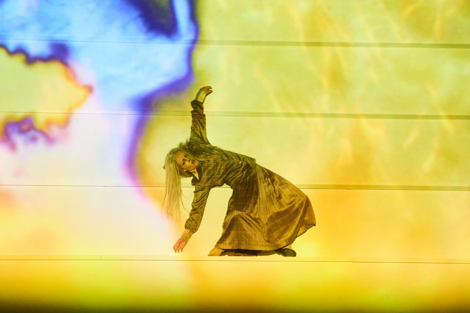 Tänzerin Laura Martín Rey beugt sich rückwärts und streckt ihre Arme kunstvoll Richtung Himmel auf einer Bühne, die in Flammen getaucht ist.