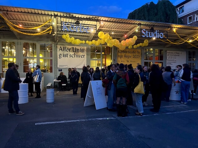 Ein beleuchteter Eingang, davor das wartende, plaudernde Publikum