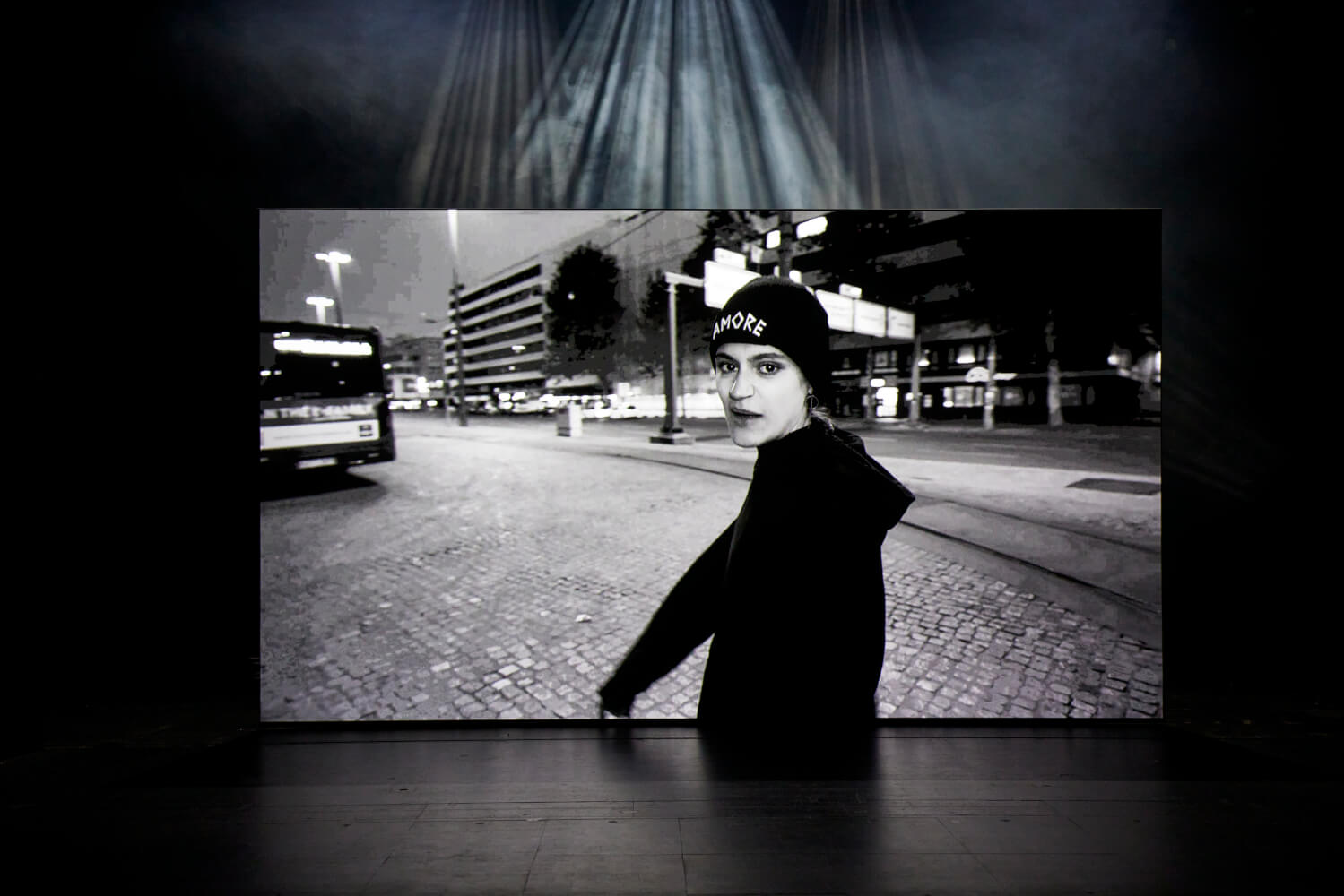 Auf der Bühne steht eine Leinwand. Darauf ist ein Film mit Darstellerin Lea Wößner zu sehen. Sie blickt direkt in die Kamera.