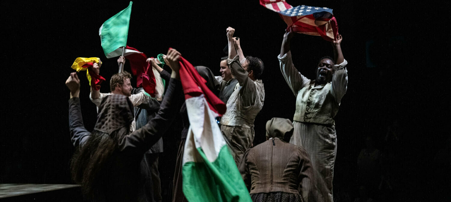 Zu sehen sind mehrere Menschen, die Fahnen schwenken auf einem Holzpodest.