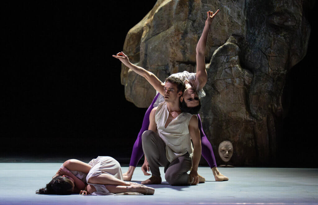 Eine Tänzerin macht eine Rückbeuge über die Schulter eines knieenden Tänzers. Neben ihm liegt eine weitere Tänzerin auf dem Boden.