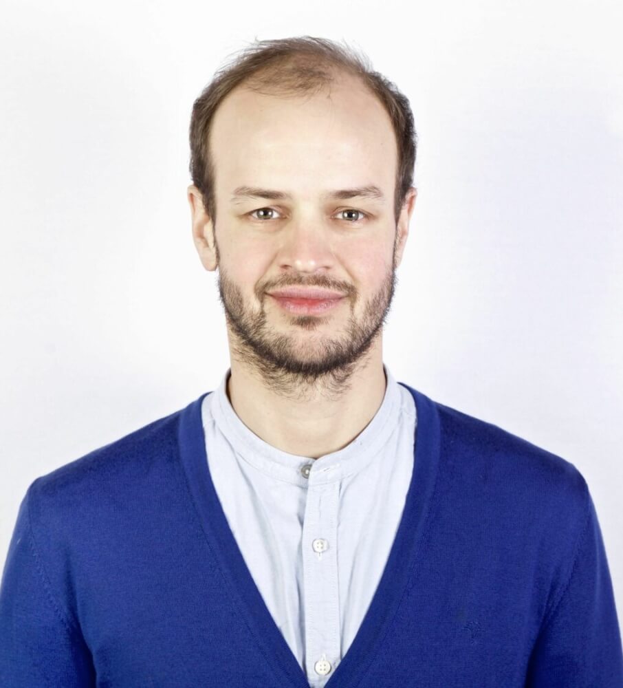 Ein Porträt von Jonas Zipf im weißen Hemd mit blauer Strickjacke.