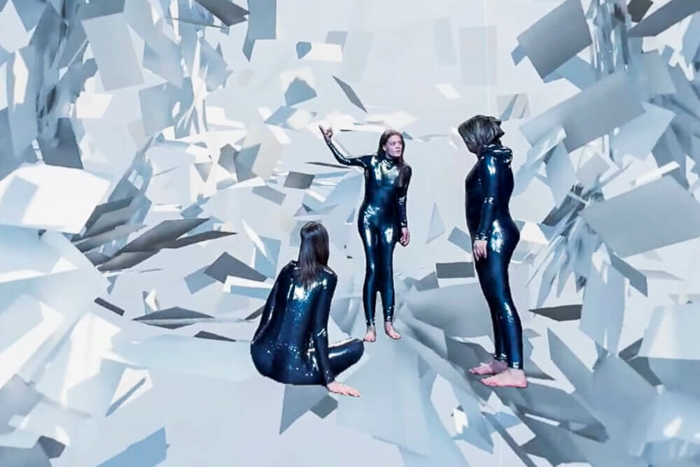 Marie Schulte-Werning, Lea Reihl und Gabriella Weber stehen inmitten einer zerfallenden Landschaft. Um sie herum ragen spitze Stücke in den Raum hinein und umzingeln sie.