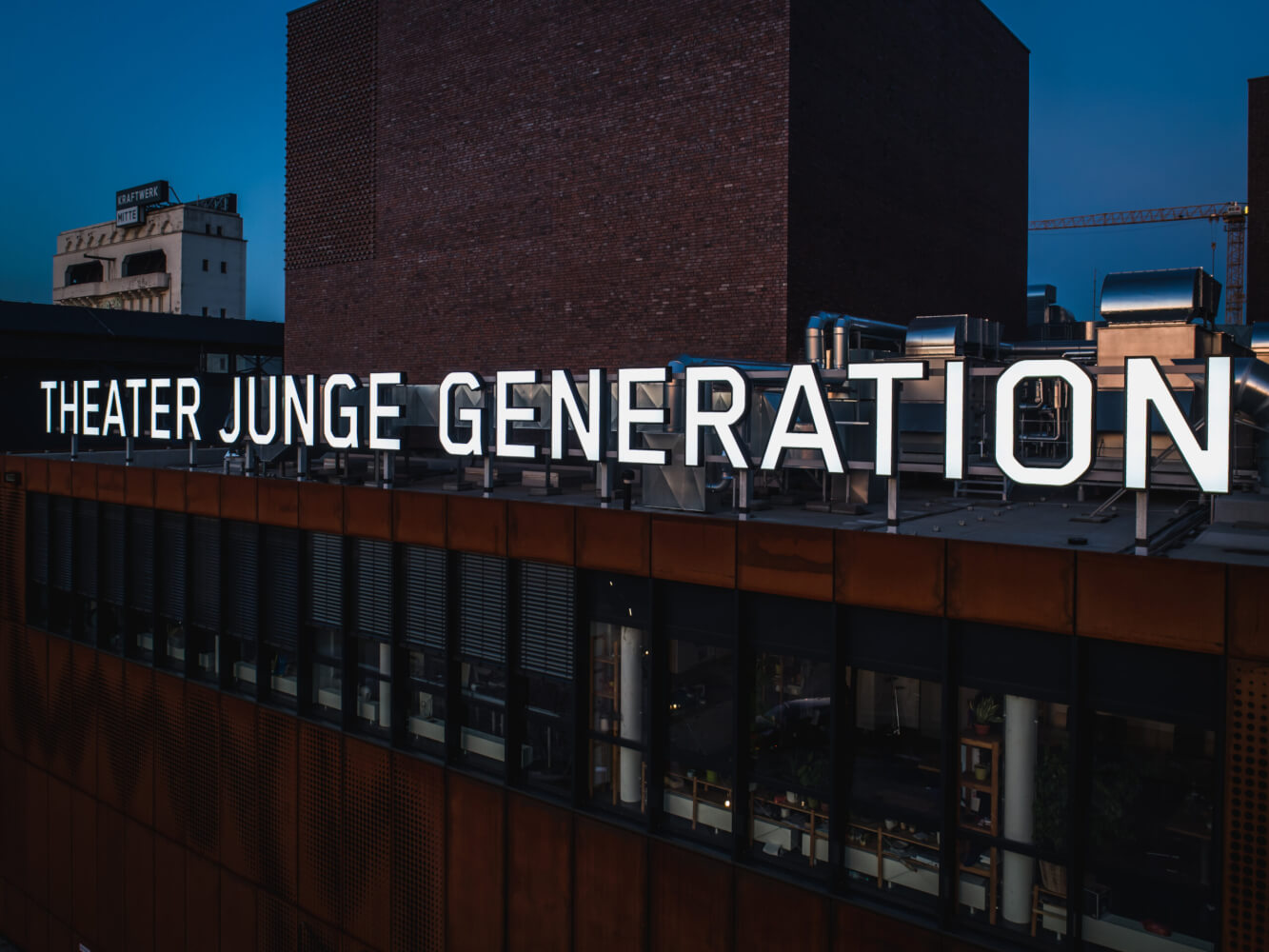 Zu sehen ist eine Nahaufnahme des Gebäudes vom theater junge generation bei Nacht. Die Buchstaben sind weiß erleuchtet.