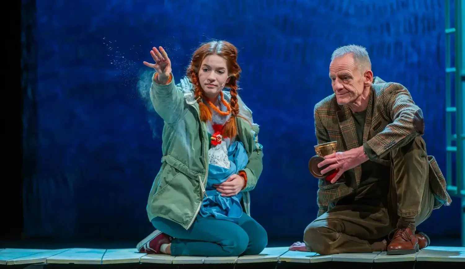 Paula (Nele Schweers) und Helmut (Michael Berger) sitzen eng beieinander auf der Bühne. Paule verstreut etwas vor sich auf dem Boden.