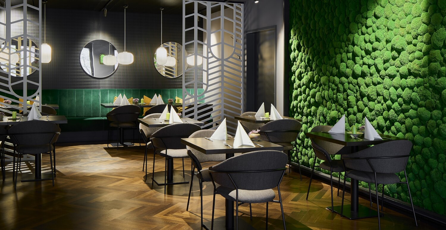 Innenansicht des Restaurants Zum grünen Kakadu, das zum Staatstheater Mainz gehört. Rechts eine mit grünem Moos besetzte Wand. Davor Zweier-Tische.