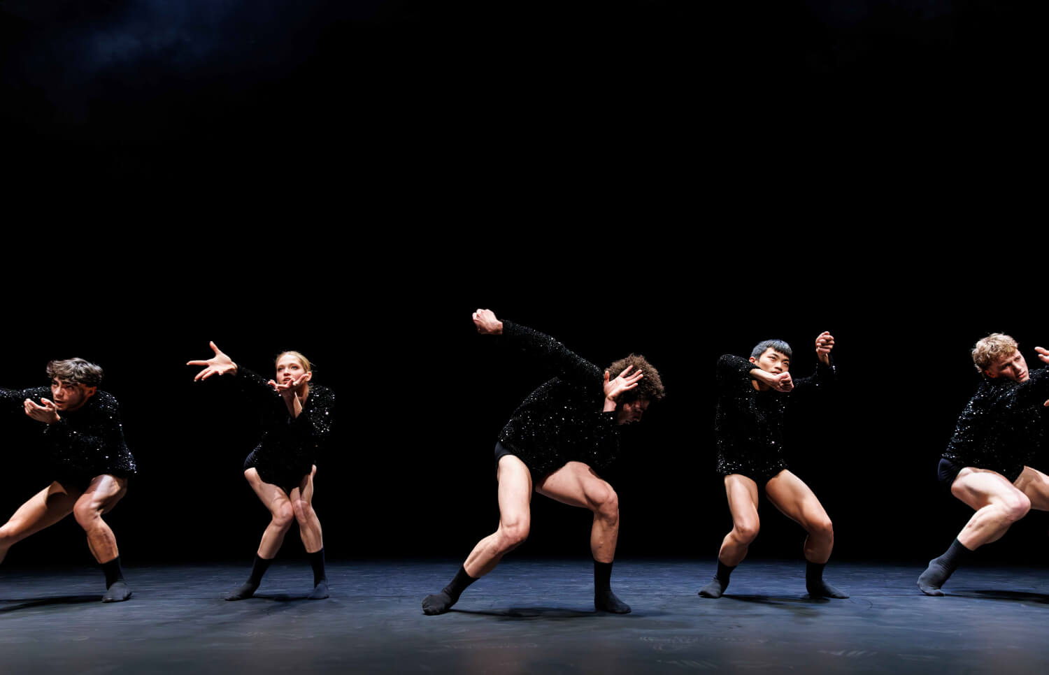 „Radical Classical“ Gauthier Dance Juniors, Choreografie von Andreas Heise. Fünf Tänzer*innen steht in einer Reihe mit nackten Beinen und schwarz-glitzernen Oberteilen und verrenken Arme und Beine.