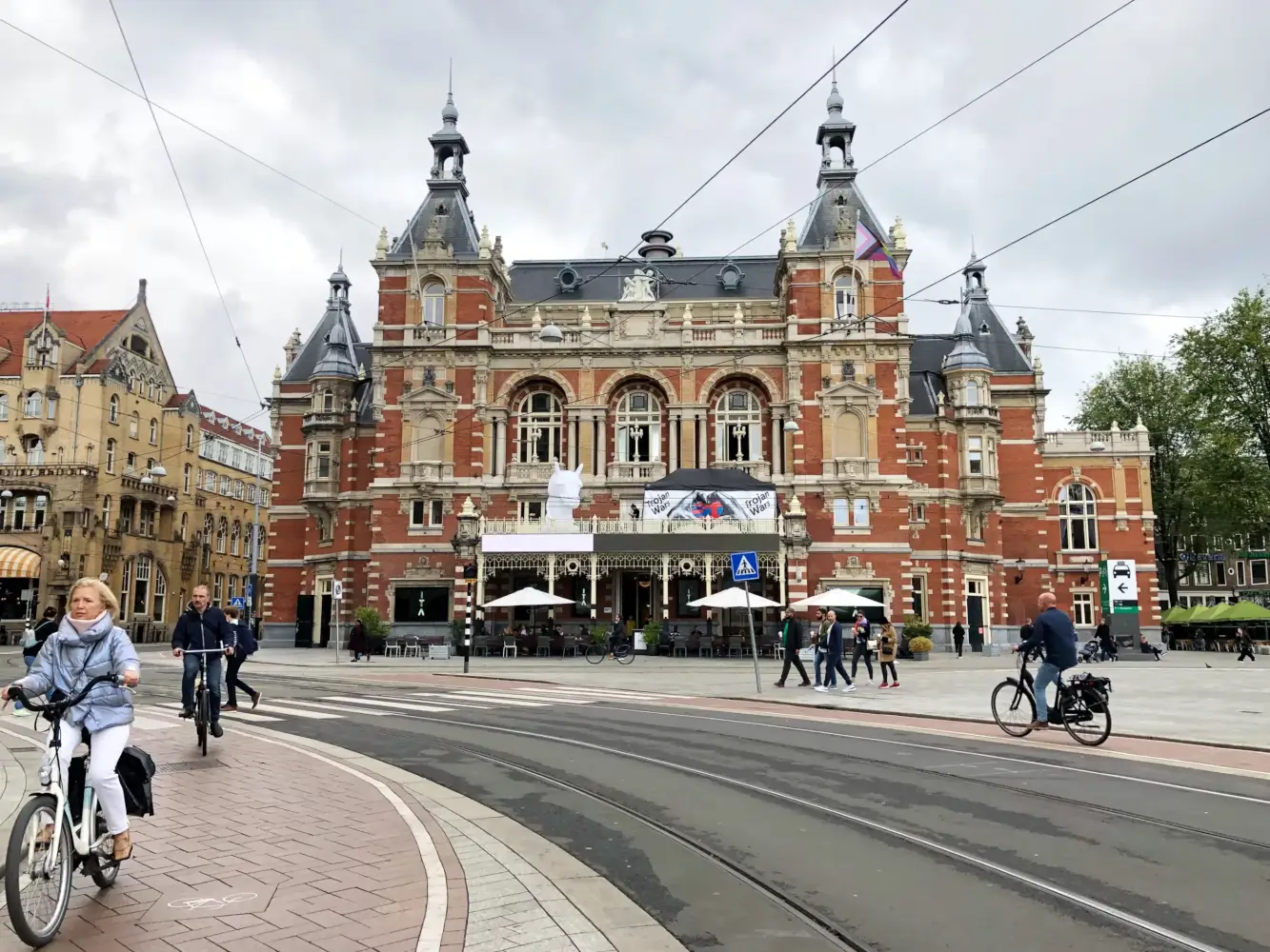 Das Internationaal Theater Amsterdam (ITA). Das Gebäude hat mehrere Turmspitzen. Davor liegt eine Straße, die nach links abbiegt. Mehrere Fahrradfahrer sind zu sehen.