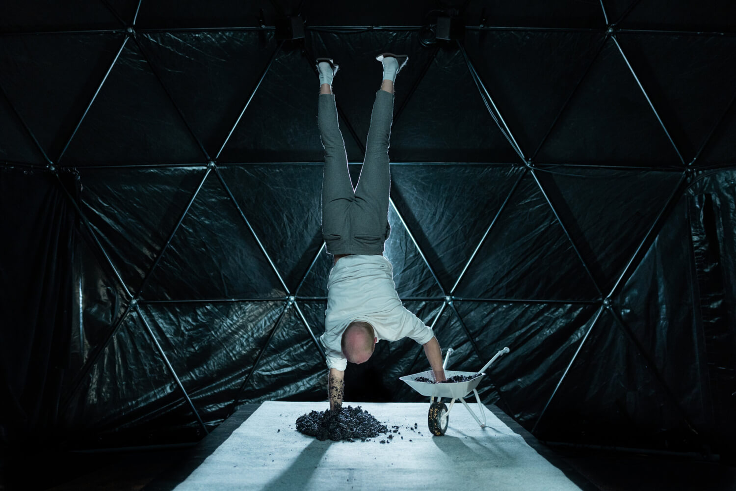 Kolja Huneck in „Symbiosis“ bei den Ruhrfestspielen in Recklinghausen. Ein Mann macht einen Handstand. Ein Arm steckt in einem nassen Erdhaufen, der andere Arm in einer kleinen Schubkarre.