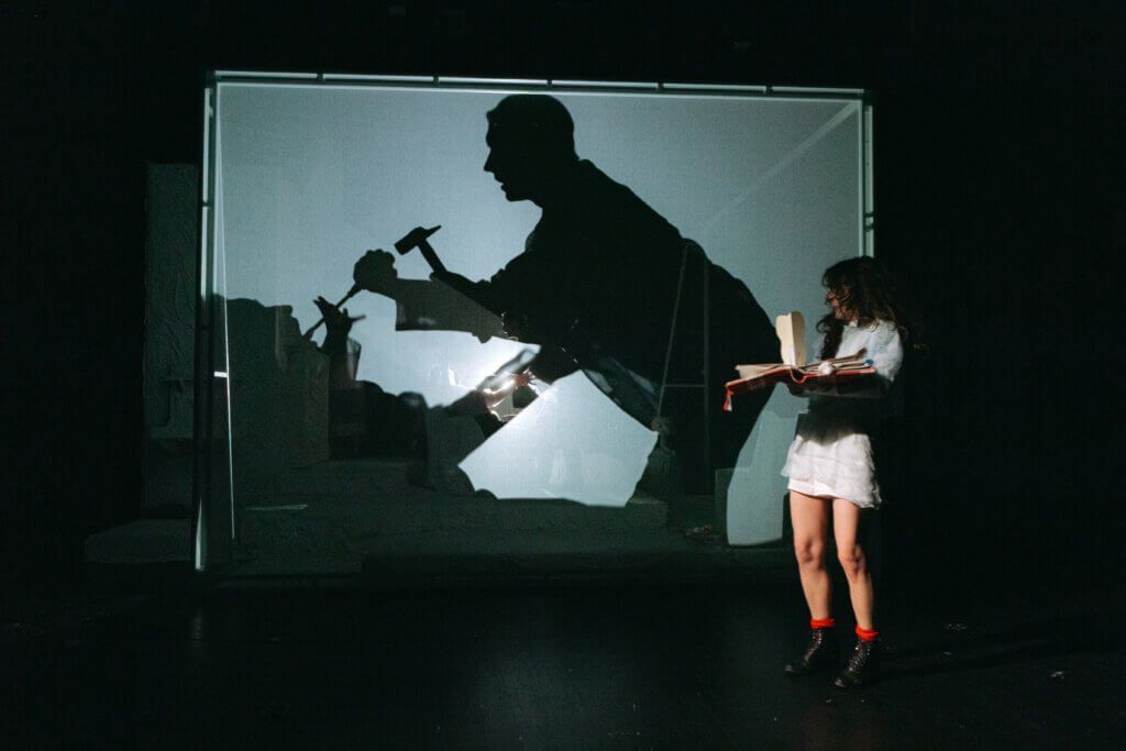 Paula Püschel und Kevin Wilke lassen hinter einer Leinwand als Schatten die Gedanken von Anne Frank (Julia Meier) Wirklichkeit werden. Julia Meier steht rechts vor der Leinwand mit ihrem Pop-up-Tagebuch in den Händen.