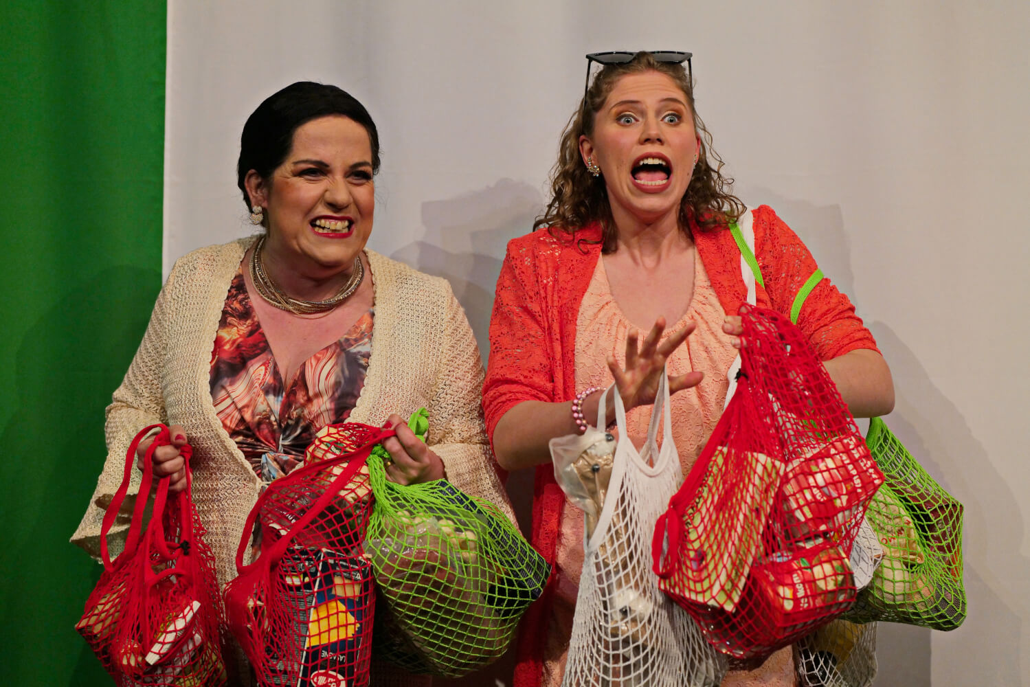 Aufführungsfoto von „Bezahlt wird NICHT!“ von Dario Fo und Franca Rame am Harztheater. Zwei Frauen stehen nebeneinander mit weiß, rot, grünen Einkaufsnetzen in der Händen.