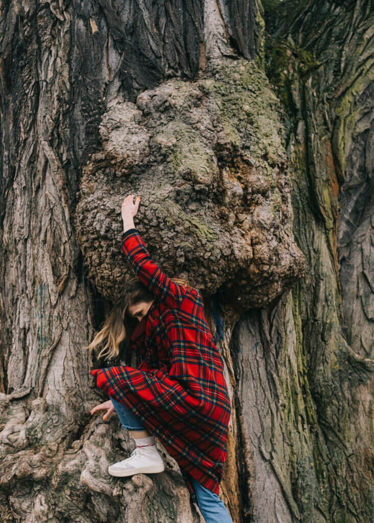 Julischka Eichel im Park in Berlin-Weißensee. Eine junge Frau steht vor einem riesigen Baum mit einem großen, runden Auswuchs. Sie stemmt sich dagegen.