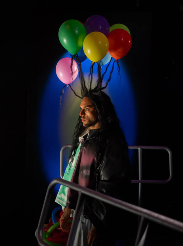 Eine Person, deren Haare nach oben stehen, weil sie an Ballons befestigt sind