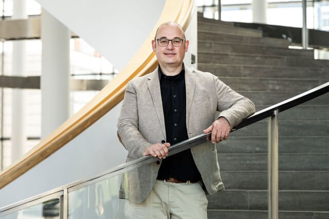 Porträt von Christian Illgen, Interimsintendant am Theater Erfurt, stehend auf einer steinernen Wendeltreppe, die Hände auf dem Handlauf abgelegt.
