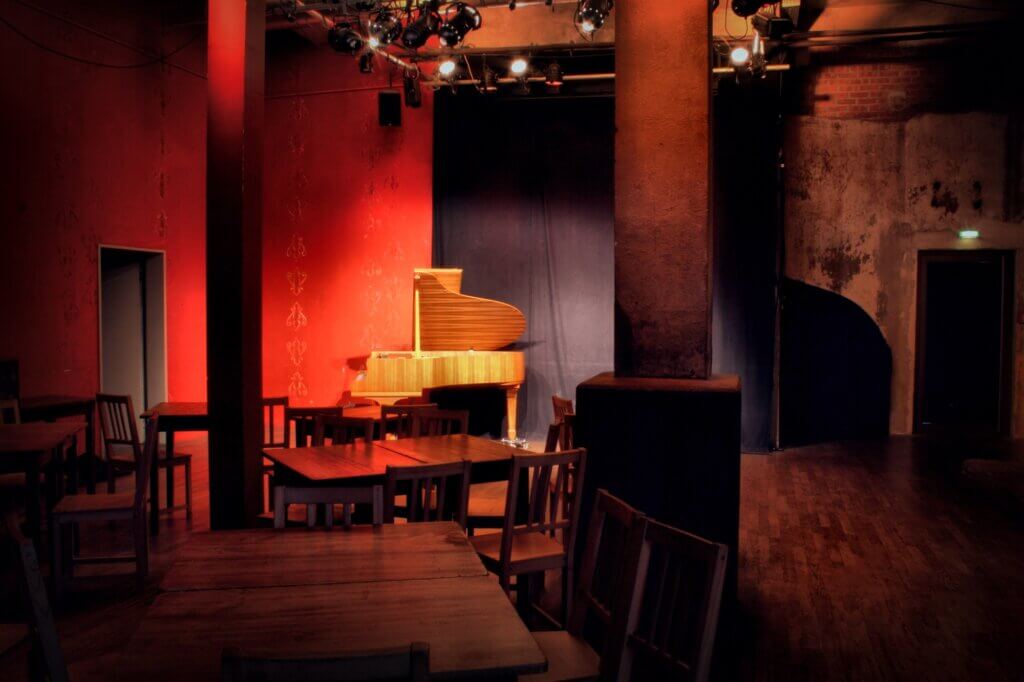 Die Kellerbar des Consol Theaters. Stimmungsvoll beleuchtet, steht an der Wand ein Flügel, davor Holztische und Holzstühle.