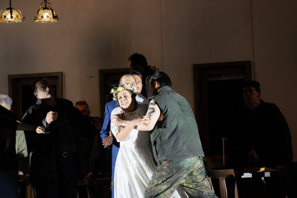 Aufführungsfoto von „Tancredi“ von Gioachino Rossini an der Oper Frankfurt. Eine Frau mit Blumenkranz auf dem Kopf und in einem Brautkleid wird von einem Mann bedrängt. Hinter ihr stehen zwei andere Männer.