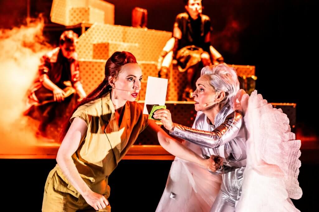 Aufführungsfoto von „Wo die Götter kauern wie Hunde“ von Leon Engler am Theater Heilbronn. Eine ältere Frau rechts hält einer jüngeren Frau ein Foto vors Gesicht, sie schaut regungslos am Foto vorbei.