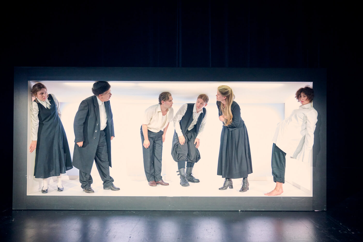 Aufführungsfoto von „Hiob“ nach Joseph Roth am Landestheater Tübingen. Sechs Menschen stehen gebückt in einem länglichen Rechteck, dass hell ausgeleuchtet ist und schauen sich an.