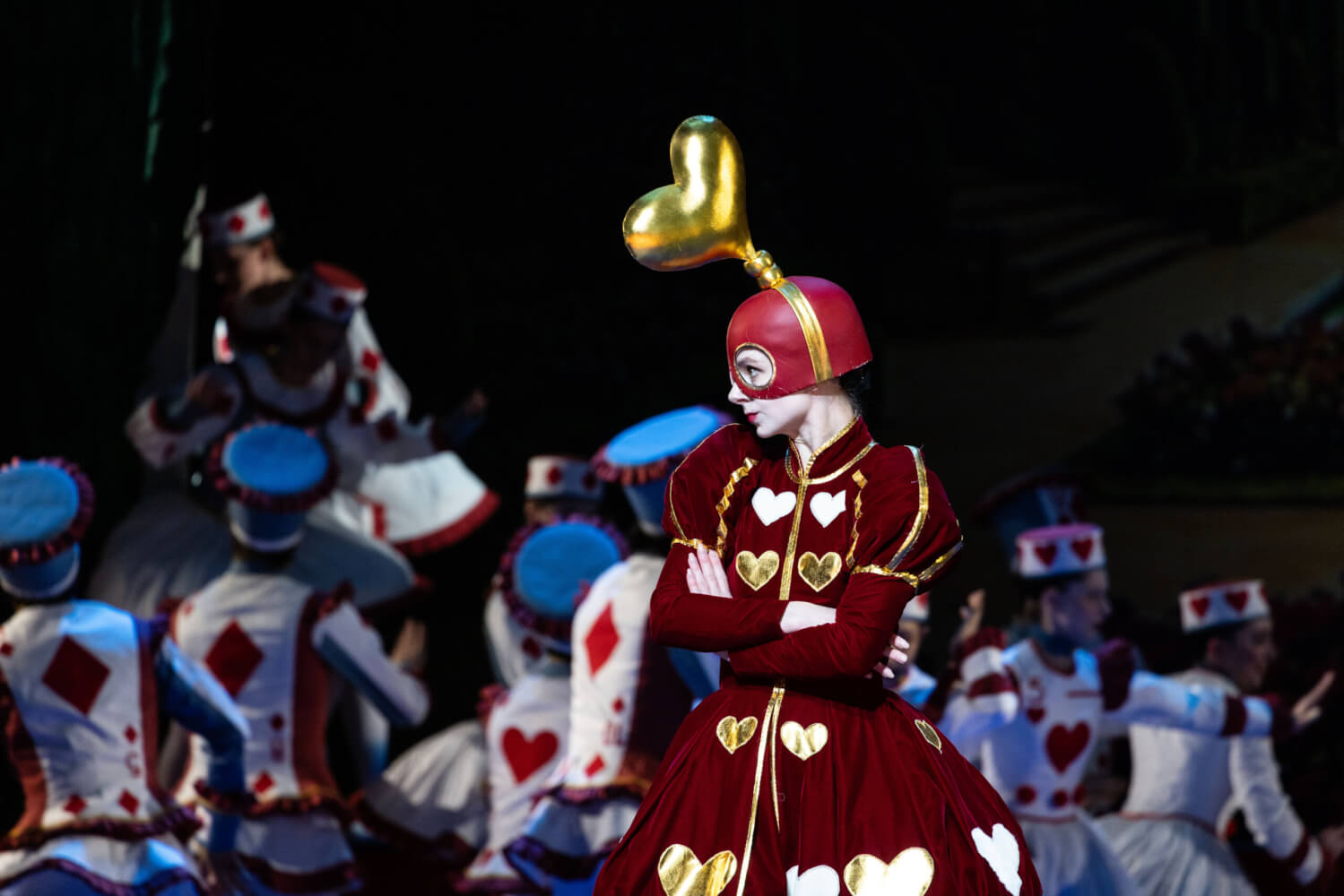 Aufführungsfoto von „Wunderland“ von Alexei Ratmansky des Hamburg Ballett an der Staatsoper Hamburg. Eine Frau in einem roten Spielkartenkleid verschränkt die Arme und schaut streng nach links.