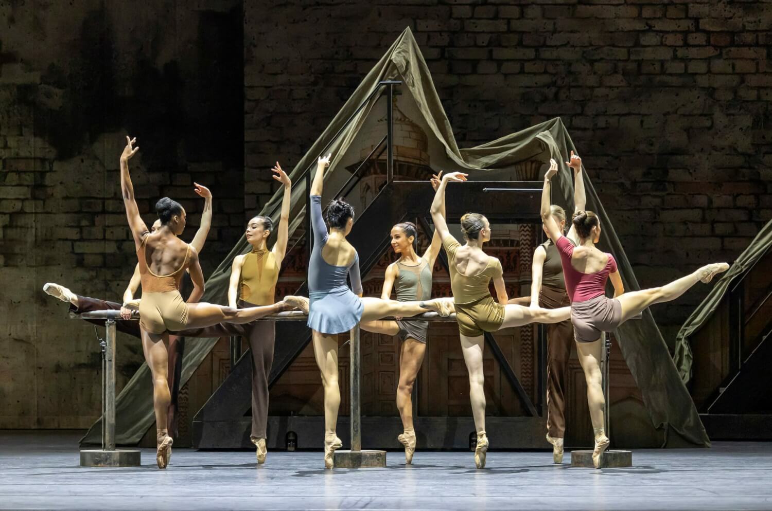 Die Tänzerinnen stehen wie in einer Ballettstunde an der Stange und heben die Beine.