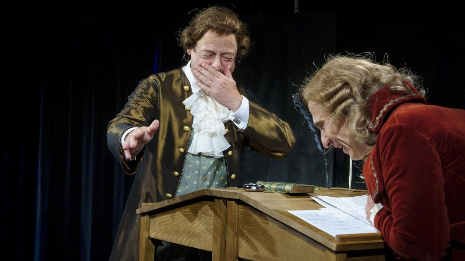 Schiller und Goethe stehen sich an einem Pult gegenüber, tauschen sich über Texte aus und lachen gemeinsam.