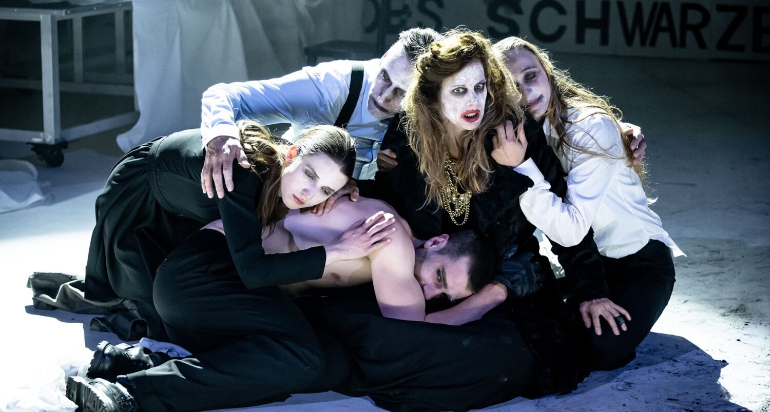 Aufführungsfoto von „Orestie“ von Robert Icke am Theater Vorpommern. Fünf Menschen, mit weißgeschminkten Gesichtern kauern dicht beieinander und halten sich fest.