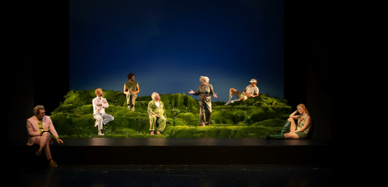 Das Ensemble steht nebeneinander auf der Bühne. Mit Himmel und Wiese auf dem Boden.